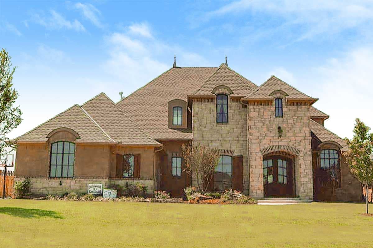 House plan exterior. Two-story, French Provincial style home. Features include arched entry, gabled rooflines, and multiple dormers.