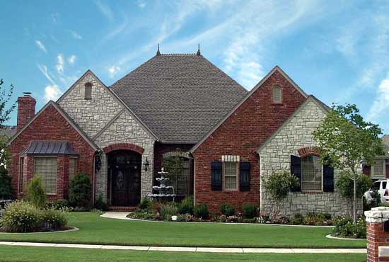 House plan exterior with brick and stone facade, asymmetrical gables, central peaked roof, and arched entryway.