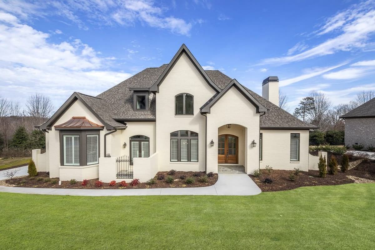 House plan exterior. Two-story home with gabled roof, arched entry, dormers, and bay window. Features include a brick exterior, and a walkway.