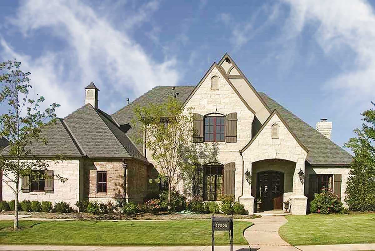 House plan exterior: Two-story stone and brick home with multiple gables, arched entryway, dormers, and decorative shutters.