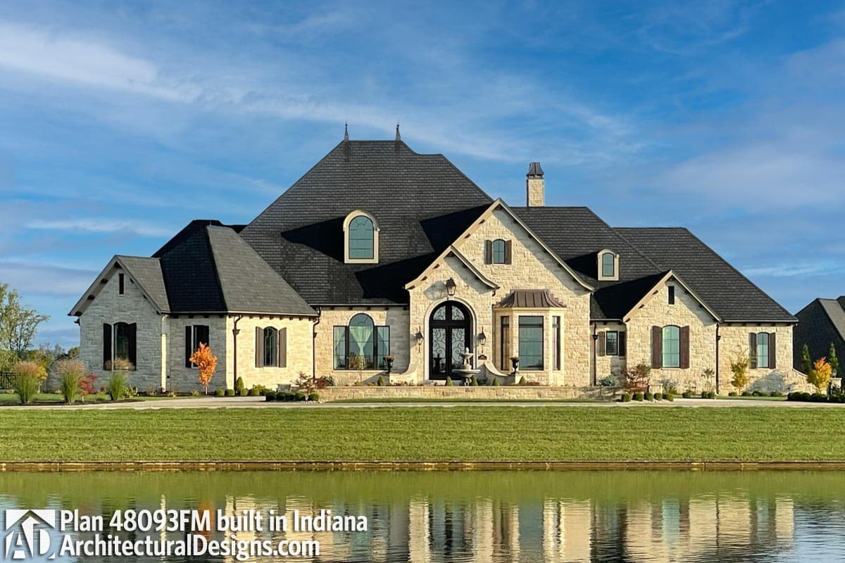 House plan exterior with stone facade, multiple gables, arched windows, and a prominent central entrance.