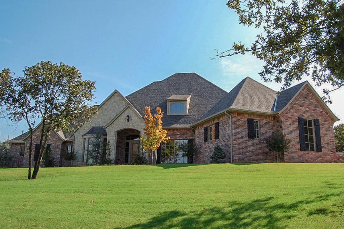 House plan exterior: Brick and stone facade, multiple gables, arched entryway, and dormer window.