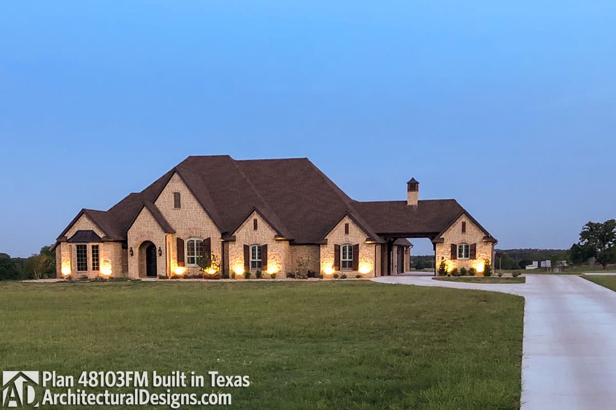 House plan exterior featuring stone facade, multi-level rooflines, prominent gables, arched entryways, and an attached porte-cochère.