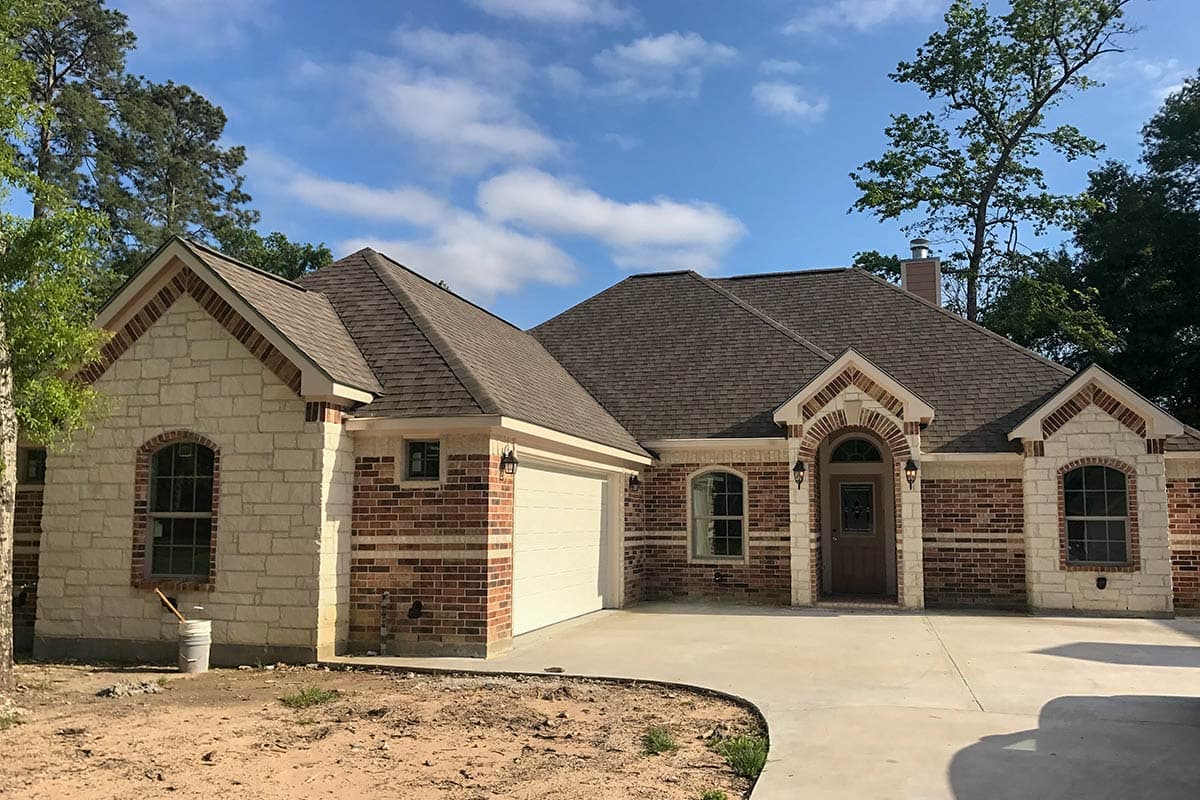 House plan exterior. One-story Ranch style home with brick and stone veneer. Features include a side-entry garage, gabled roof, and arched entryway.