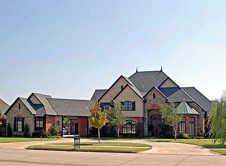 House plan exterior: Stone and brick two-story residence with a porte-cochère, multiple gables, and a circular driveway.