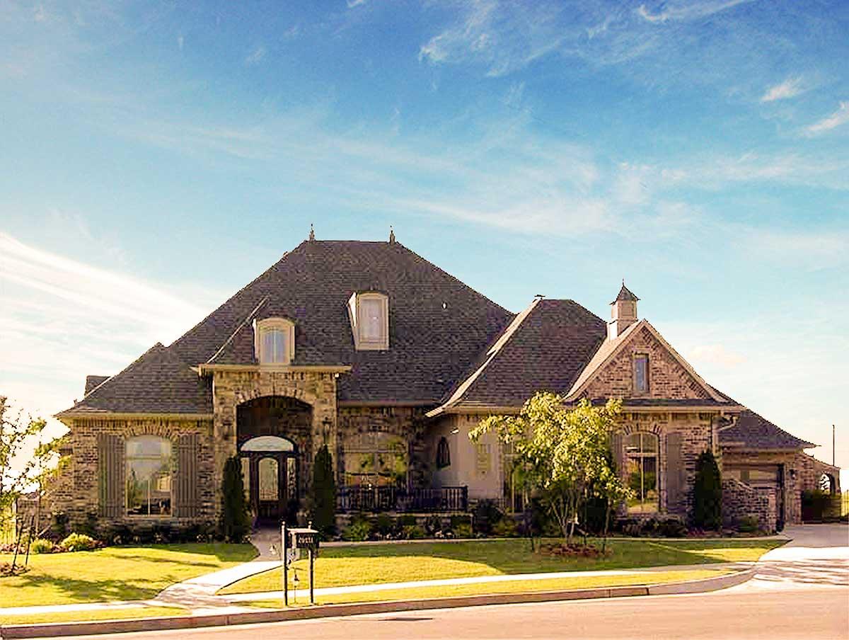 House plan exterior: Two-story stone house with arched entryway, prominent gables, dormer windows, and a cupola.