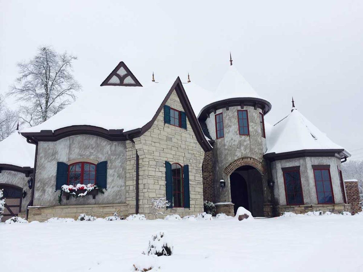 House plan exterior featuring stone and stucco with arched entry, turrets, multiple gables, and dormers under snow.