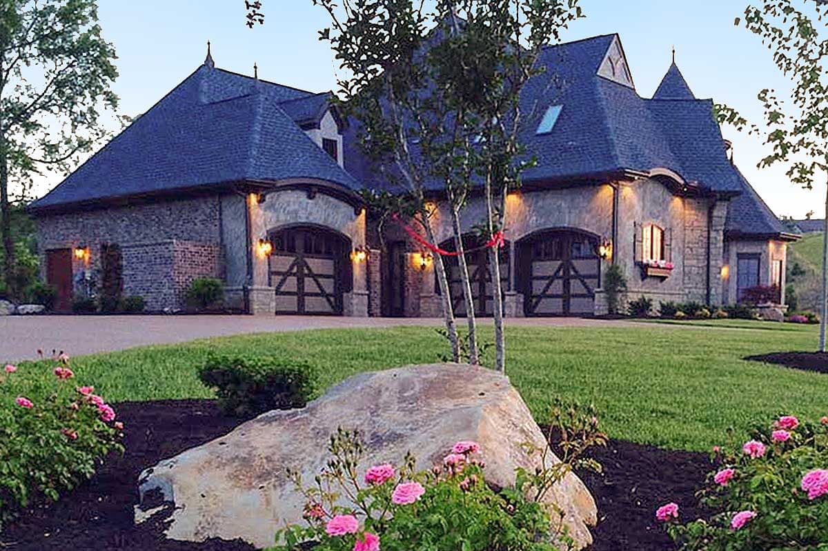 House plan exterior with multiple arched garages, stone accents, and steeply pitched dark roof.