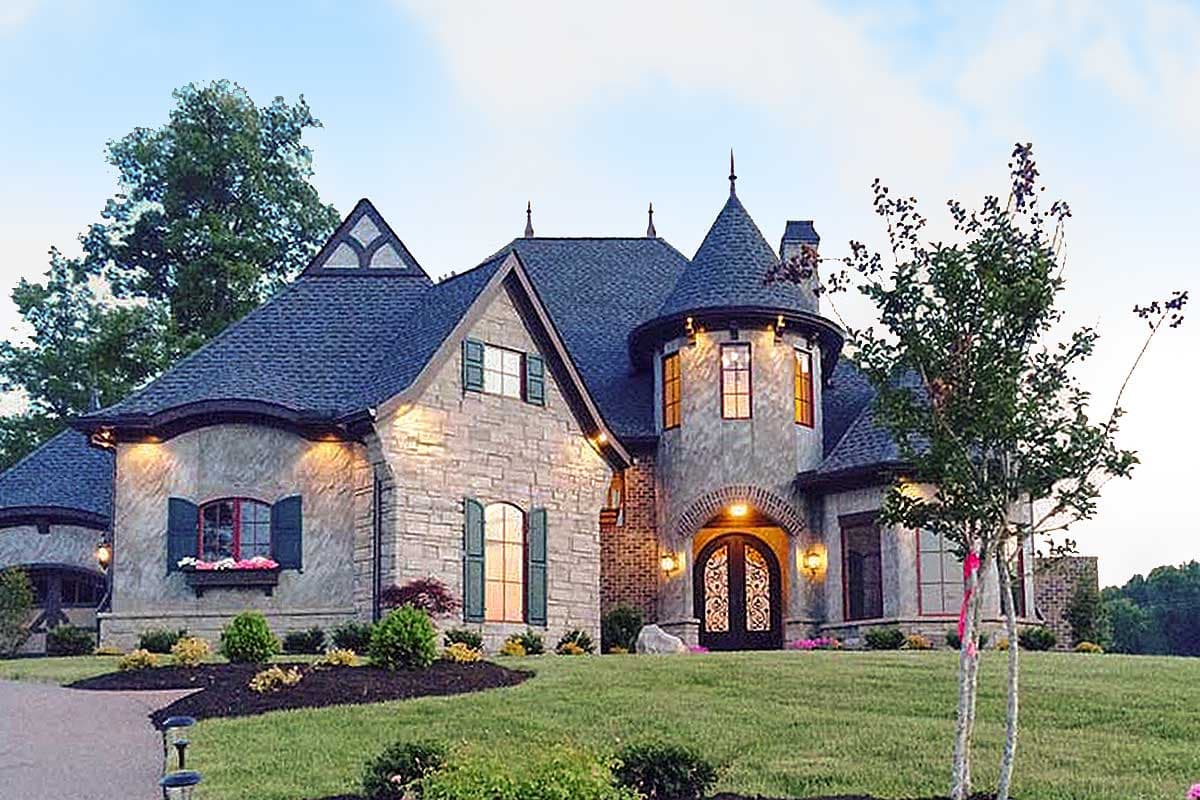 House plan exterior featuring a castle-like turret, stone facade, gables, and arched double doors.