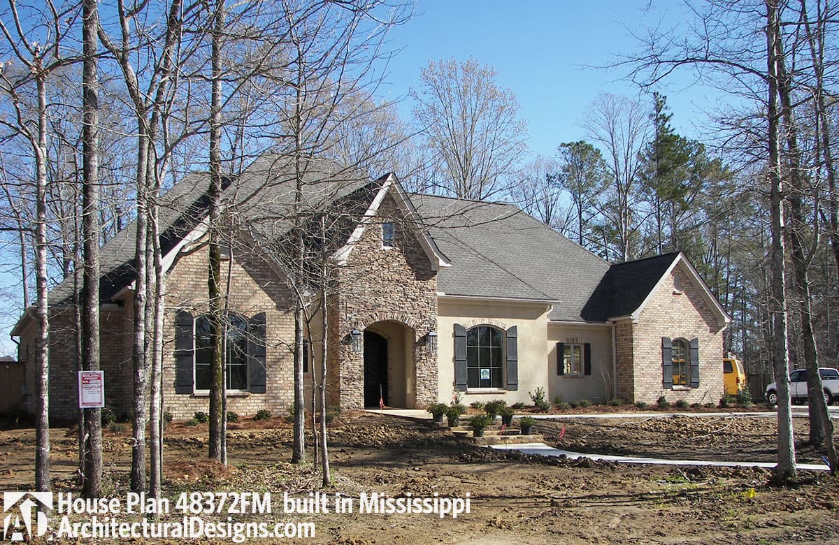 House plan exterior: Single-story home with brick and stucco, arched entryway, gables, and multiple dormers.