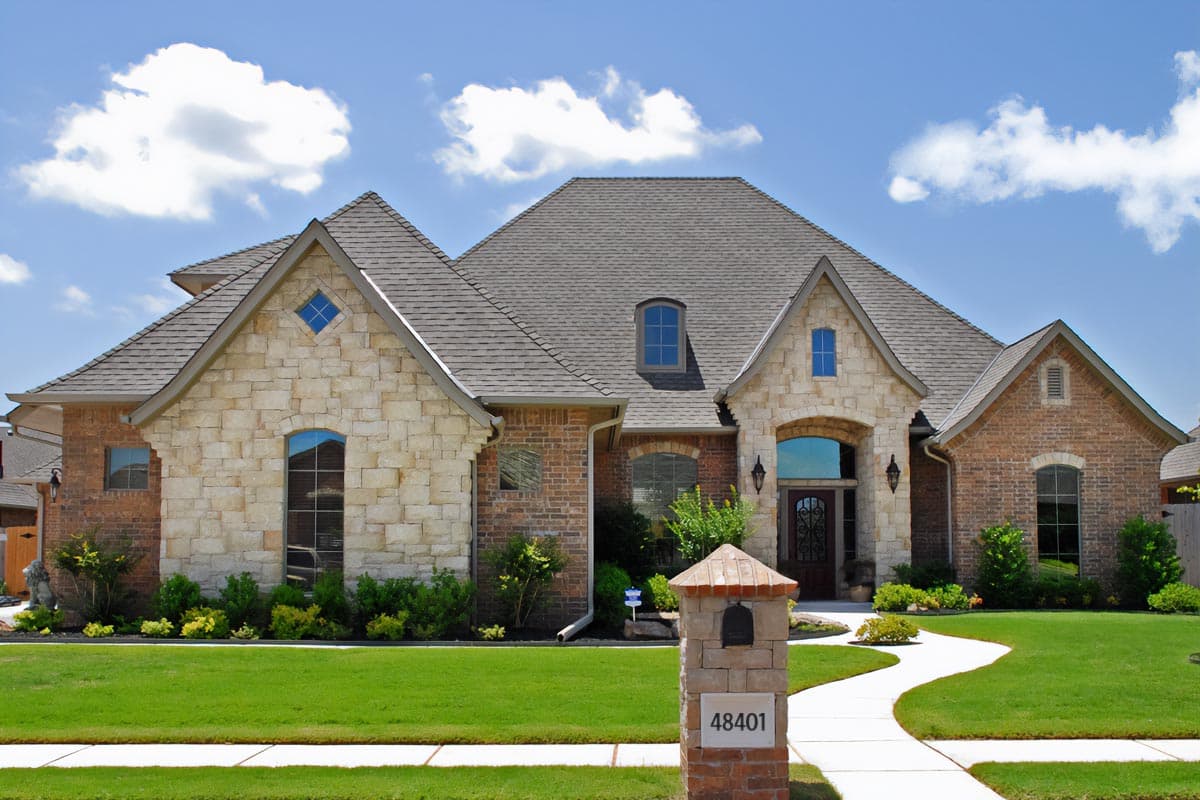 House plan exterior: Two-story home with brick and stone facade, arched entryway, multiple gables, and dormer window.
