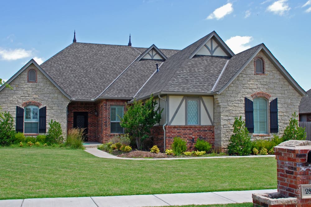 House plan exterior featuring stone and brick facade, multiple gables, dark shutters, and peaked dormers.