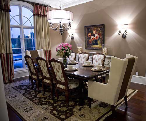 Dining room with large arched window, dining table set for eight, ornate chandelier, and wall sconces.