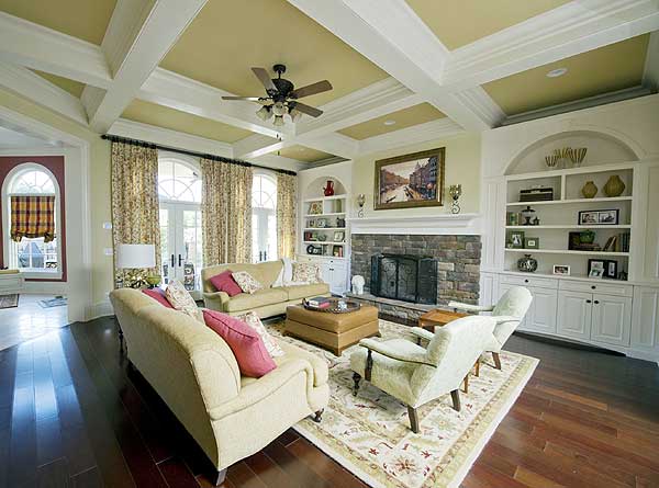 Living room with coffered ceiling, stone fireplace, built-in shelving, and large windows.