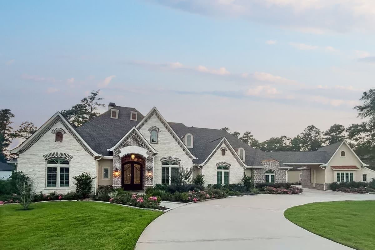 House plan exterior. Two-story home with a brick and stone facade. Features include multiple gables, arched windows, and a porte-cochère.
