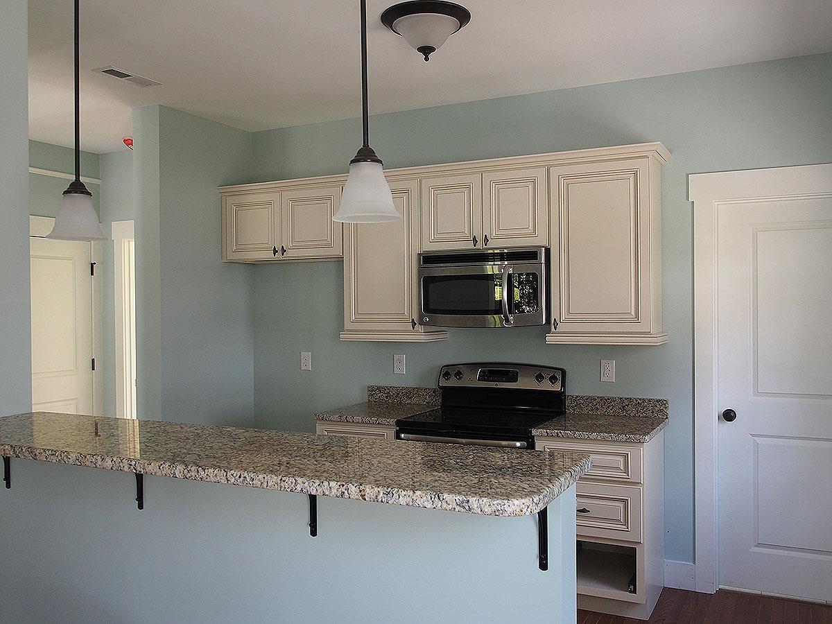 Kitchen with light blue walls, cream cabinets, granite countertops, stove, microwave, and breakfast bar with pendant lights.