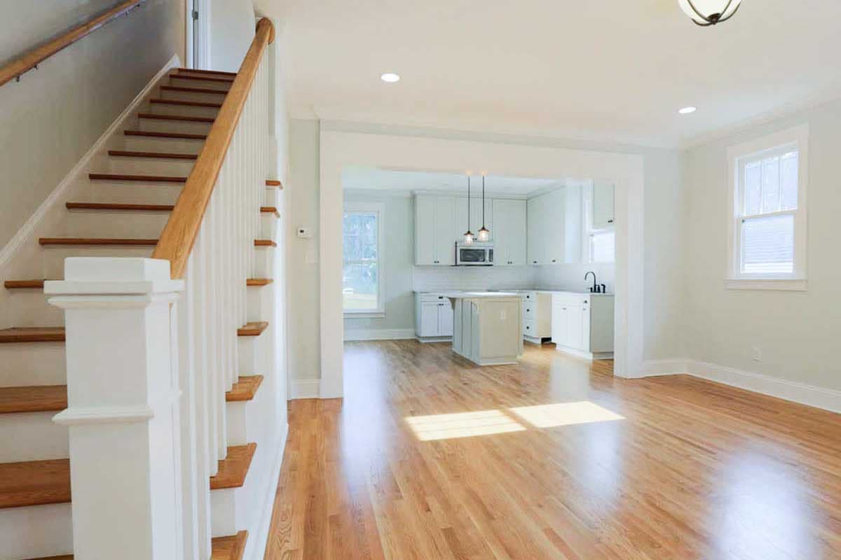 House plan interior view showing staircase, open living space, and kitchen with island, white cabinets, and pendant lights.