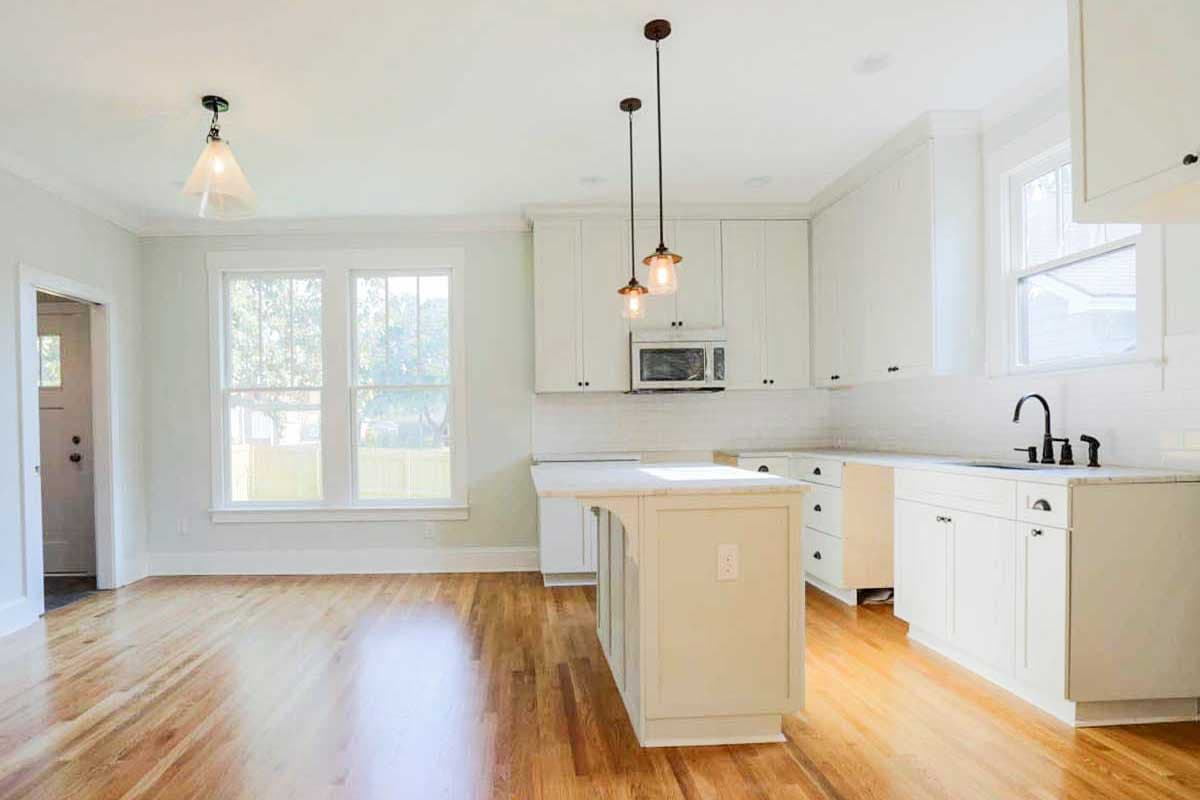 Interior view of a kitchen with white cabinets, a central island, subway tile backsplash, and hardwood floors.