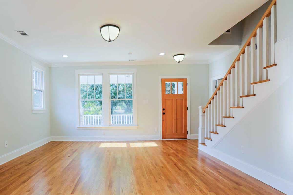 Interior view of entryway with hardwood floors, wooden door with glass panes, and a staircase with white balusters.