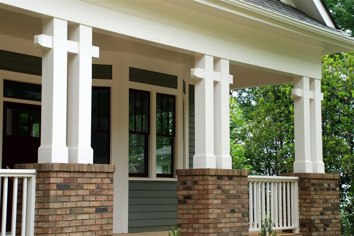 House plan exterior showing brick bases, white square columns with cross detailing, and green siding.
