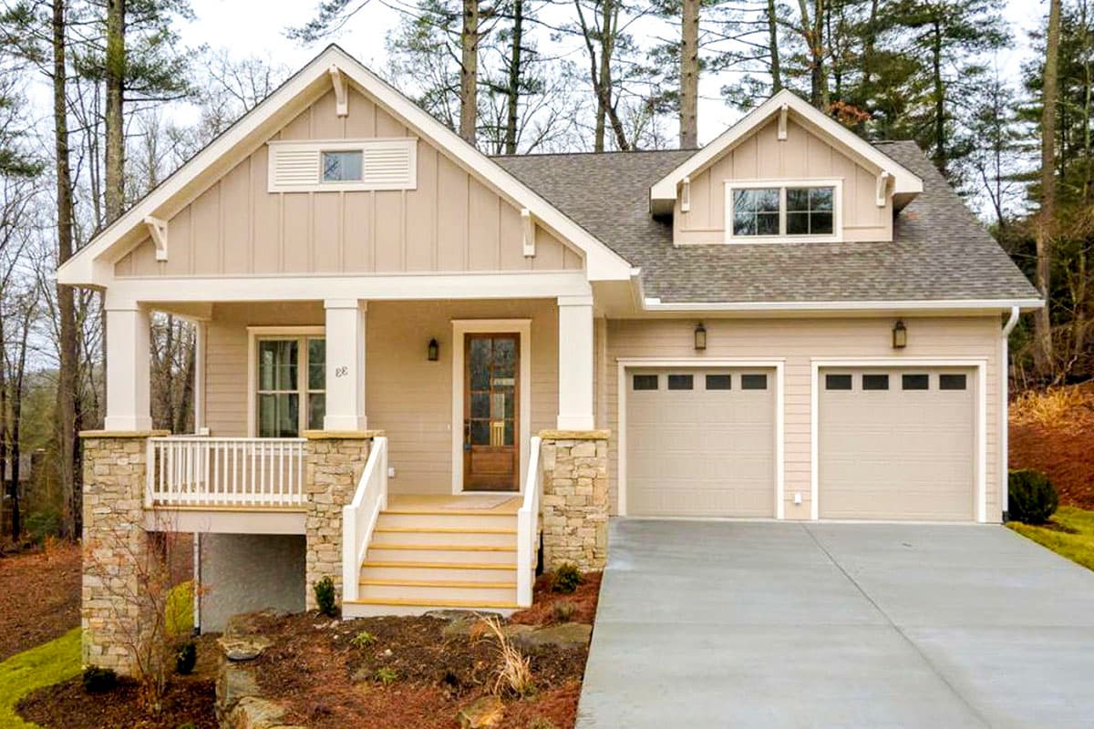 House plan exterior: Beige siding, covered front porch with stone accents, and a two-car front-entry garage.