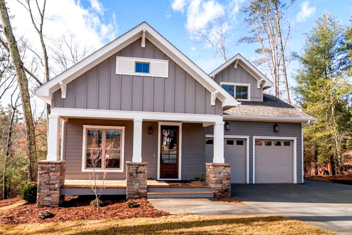House plan exterior. Craftsman style, one-story home with front porch supported by stone columns, gables, and attached two-car garage.