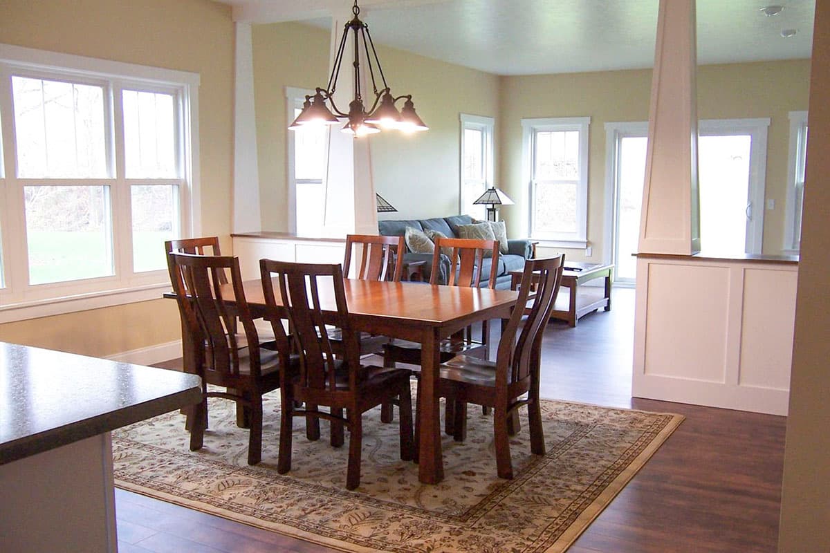 Open-concept dining area with wooden table and chairs, leading to a living room with sofa and large windows.