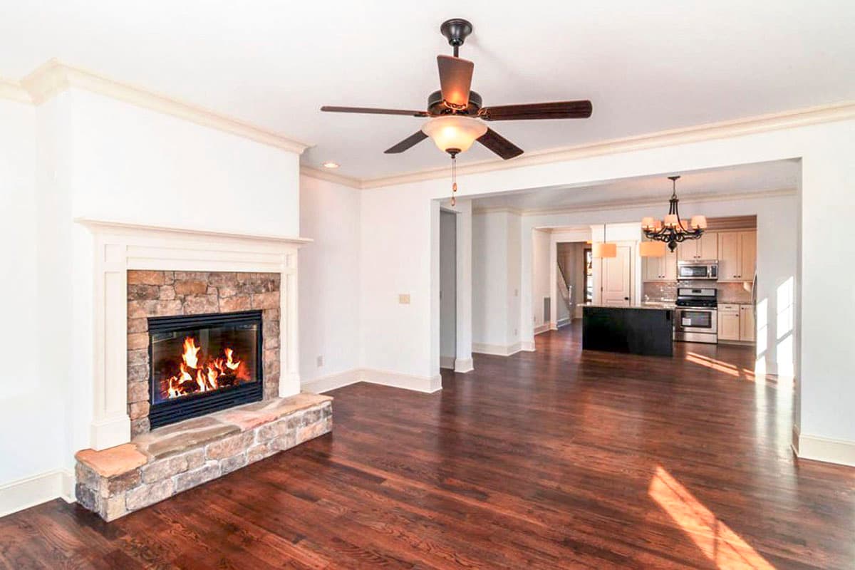 Interior view of open-concept living space with stone fireplace, ceiling fan, and kitchen with island.