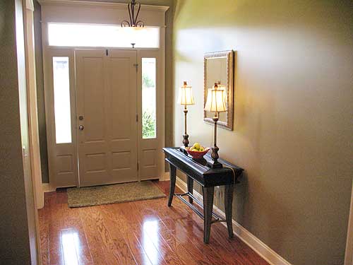 Interior view of a home entryway with double doors, sidelights, transom window, console table with lamps, and hardwood floors.