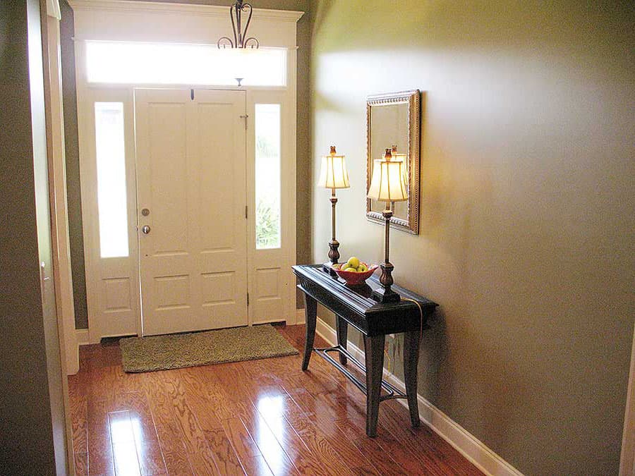 Interior view of a home entrance with double doors, sidelight windows, transom window, console table with lamps, and wood flooring.