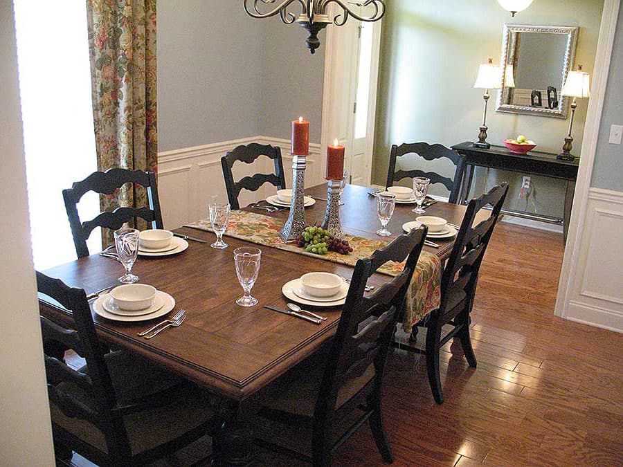 Dining room with a wooden table set for six, dark chairs, floral runner, chandelier, and a console table with lamps and mirror.