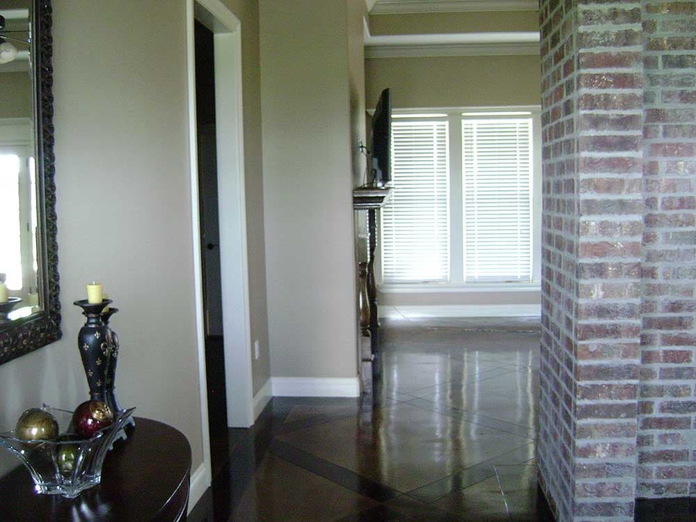 Interior view of a hallway with a decorative mirror, a brick column, and windows with blinds.