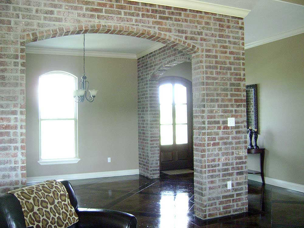 Interior view of a house with exposed brick archways, arched window, and a dark wood floor.