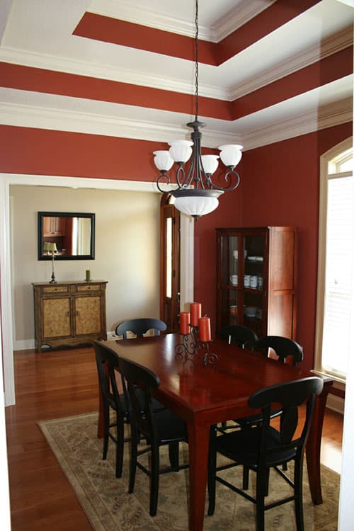 Dining room with a coffered ceiling, wood table with black chairs, glass-front cabinet, and entryway visible.