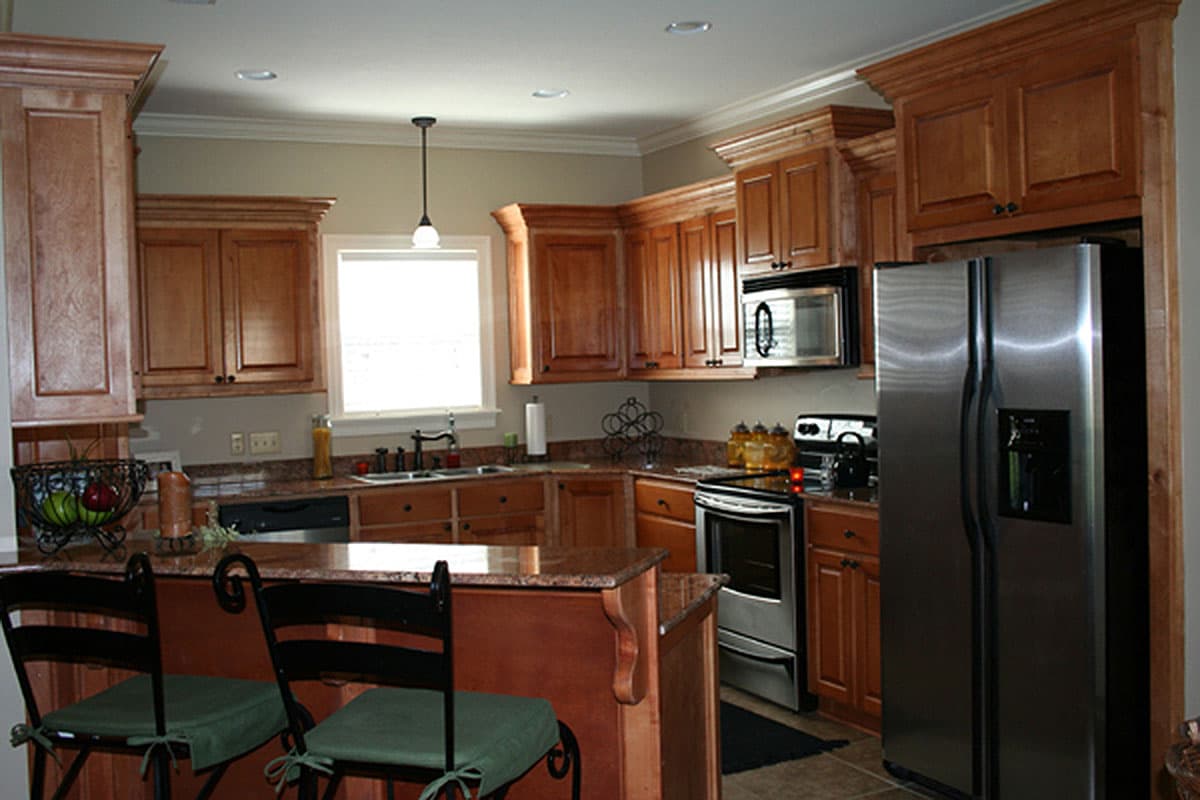 Kitchen interior with wood cabinets, granite countertops, stainless steel appliances, and a large island with bar stools.