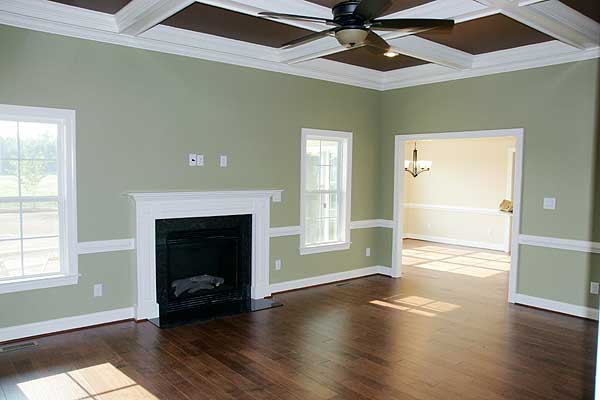 Interior view of a living room with a fireplace, coffered ceiling, ceiling fan, and view into an adjacent dining room.