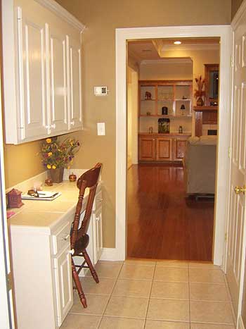 Built-in desk with white cabinetry, chair, and view into living room with wood floors and built-in shelving.