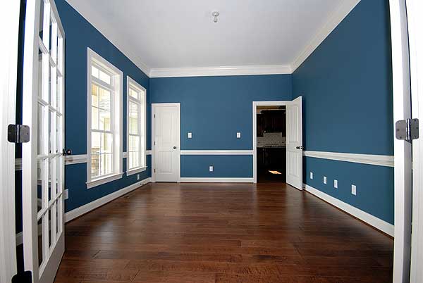 Interior view of a room with French doors, three windows, and a doorway leading to a kitchen.