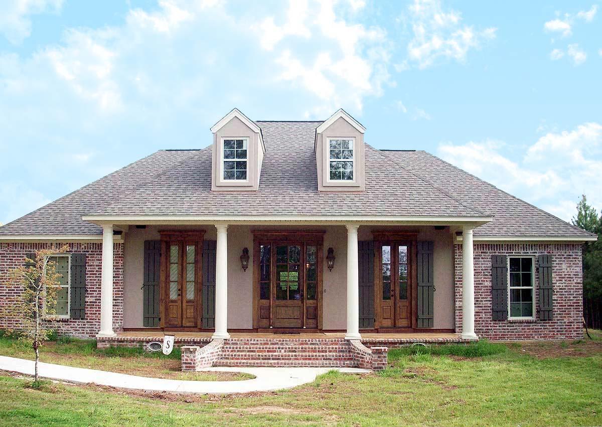 House plan exterior: One-story home with a central covered porch supported by columns, double dormers, brick facade, and wooden doors.