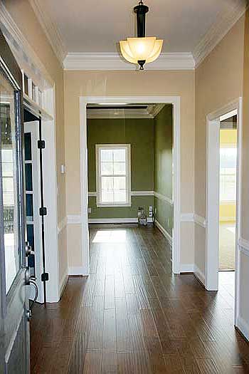 Interior view of a house hallway with crown molding, wainscoting, a pendant light, and doorways to other rooms.