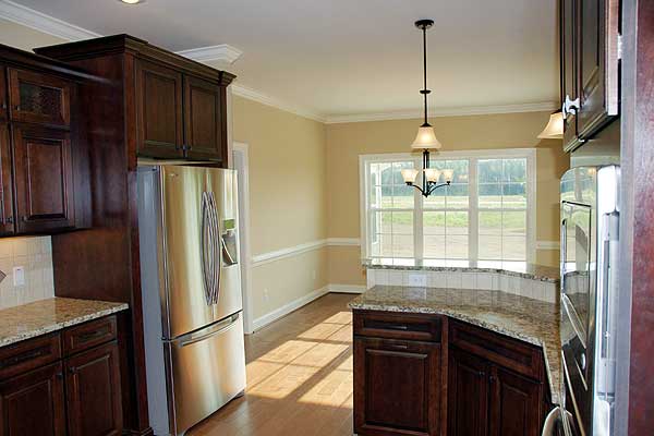 Kitchen with dark wood cabinetry, stainless steel refrigerator, granite countertops, and a dining area with large windows.