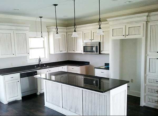 Kitchen with white beadboard cabinets, black countertops, a center island, and stainless steel appliances.