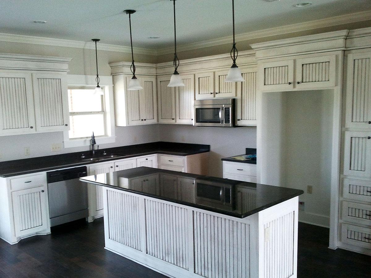Kitchen with white beadboard cabinets, black granite countertops, and a central island with pendant lighting.