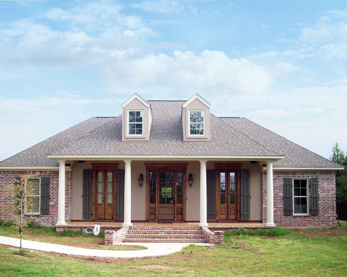 House plan exterior: one-story home with wide covered porch, brick accents, double front doors, and two dormer windows.