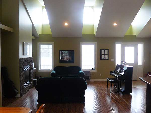 Interior view of living room with stone fireplace, two sofas, grand piano, and vaulted ceiling with skylights.