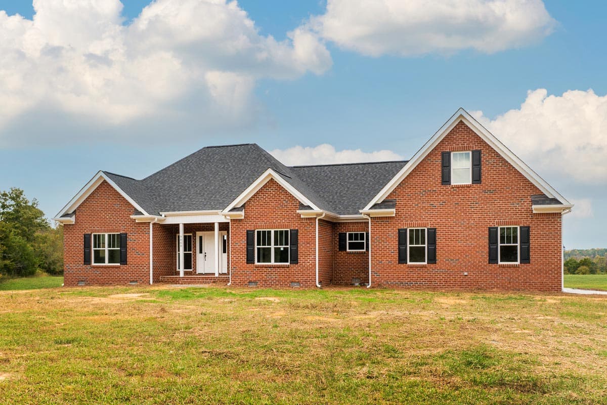 House plan exterior. One-story brick house with a gable roof, covered porch, and black shutters on multiple windows.