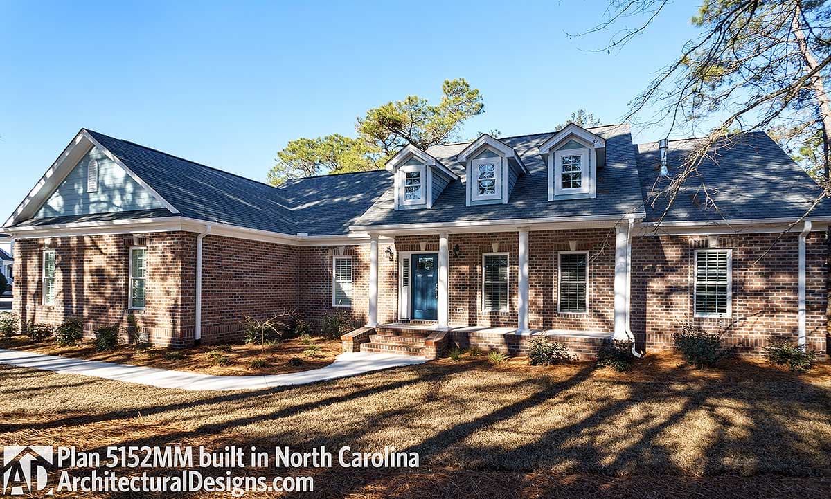 House plan exterior: Brick ranch with gabled dormers, covered porch with columns, and multi-level rooflines.