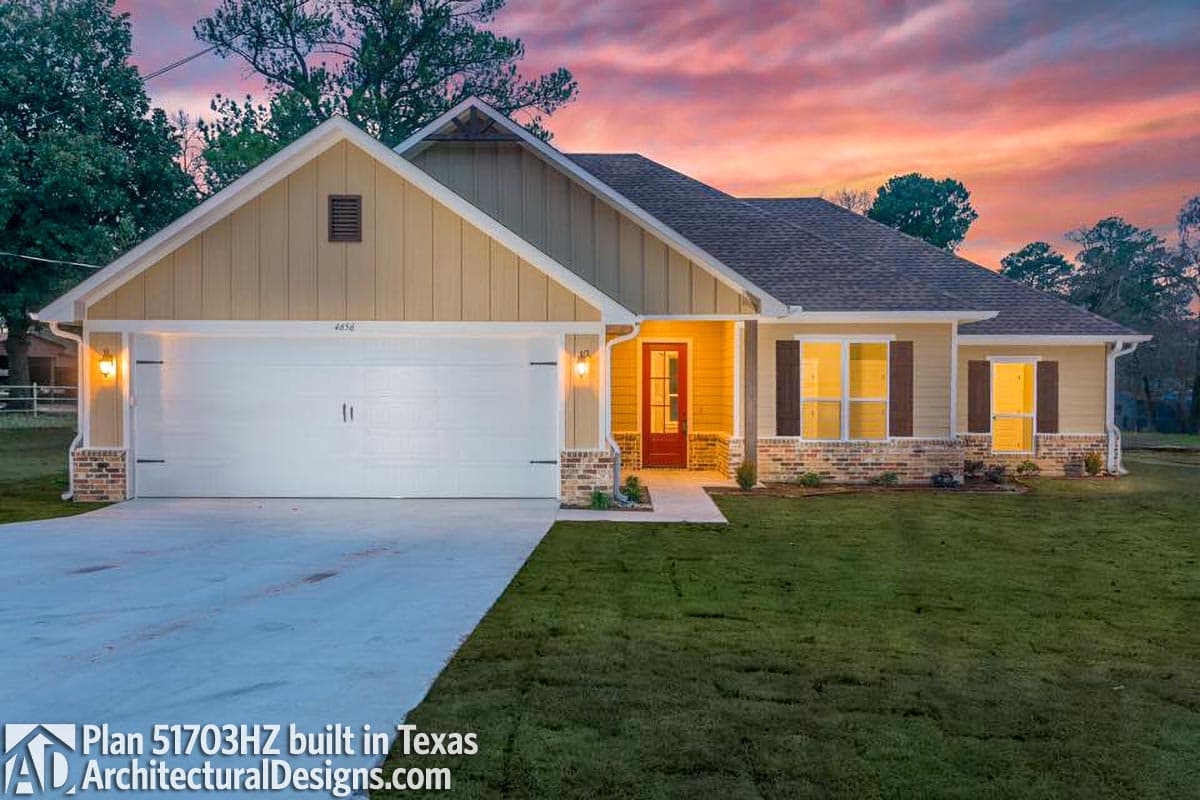 House plan exterior: one-story, tan siding, brick base, front-facing garage, gable roof, and covered entry.