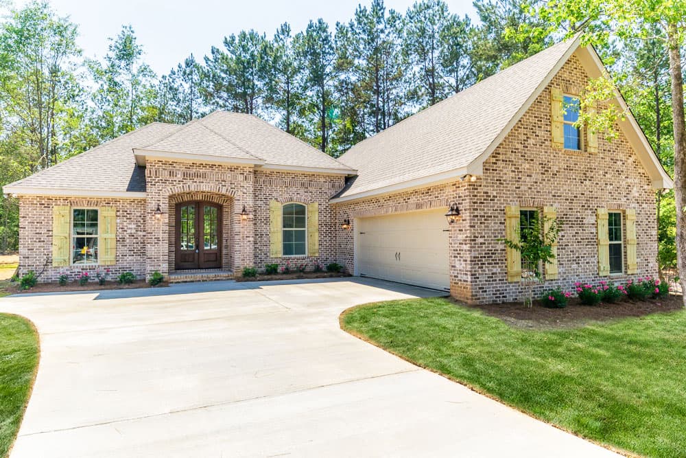 House plan exterior. One-story brick house with gabled roof, attached garage, and double front entry doors. Features window shutters.