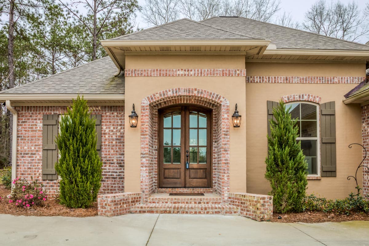 House plan exterior with brick accents, arched entry with double wood doors, and shutters on windows.